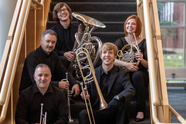 Image of 5 musicians sitting on stairs of the Center for Performing Arts. Each have a different brass instrument (Trumpet, trombone, etc.)