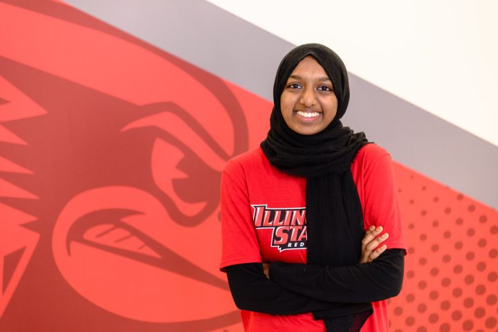Hasna Mohamed Jamal standing in front of a Reggie Redbird logo