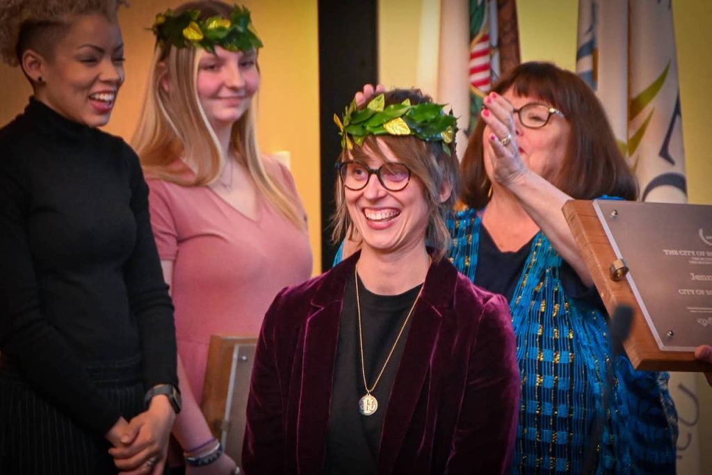 Dr. Jenna Goldsmith, ISU alum, is crowned poet laureate of Rockford, Il. She is wearing a maroon velvet blazer and a crown of leaves.