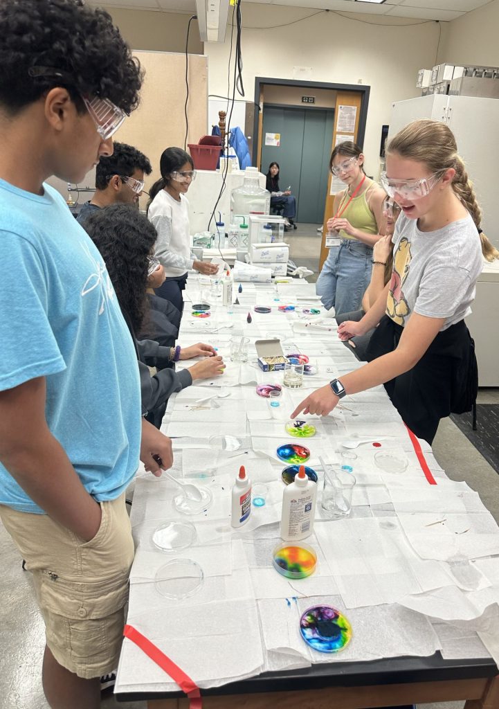 Students standing on opposite sides of a long, narrow table, conducting a science experiment