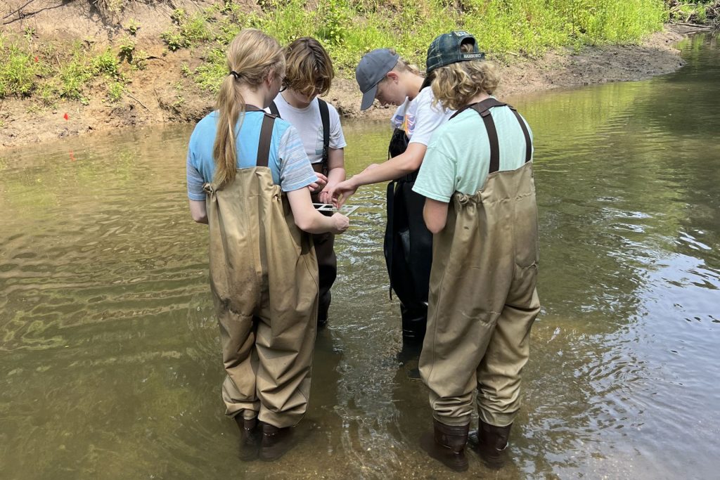 Students standing in a river examining samples.