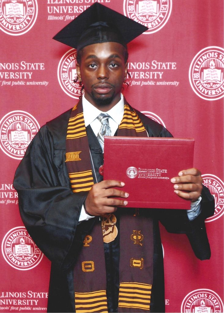 Kristian Philpotts, wearing a graduation cap and gown, holds a red Illinois State University diploma cover.