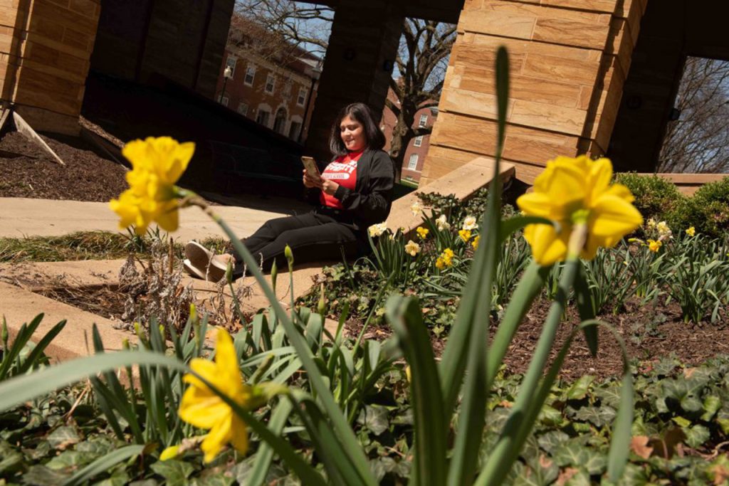 student sitting by a campus building near flowers