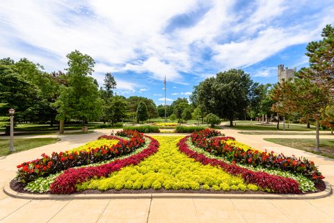 photograph of the quad with flowers, flag pole, and old main bell.