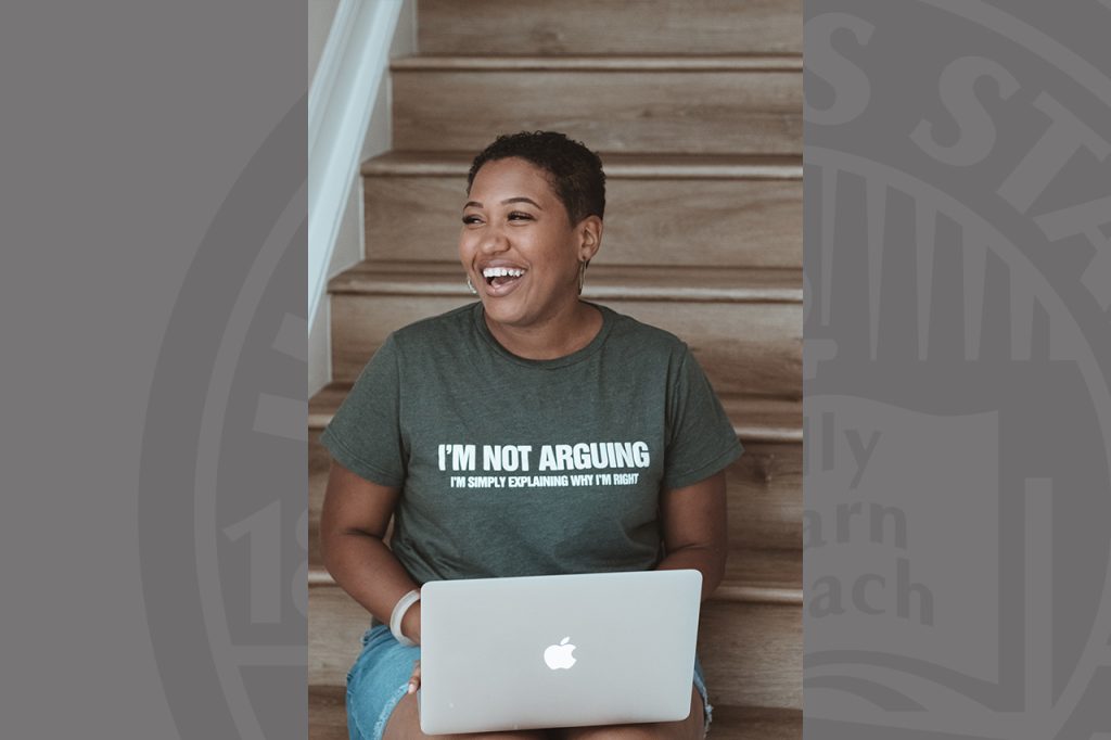 Person wearing T-shirt, sits on stairs holding laptop and smiling.
