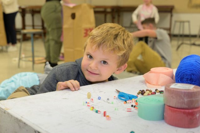 A child works with colorful beads during an artmaking activity while other children work on projects in the background.