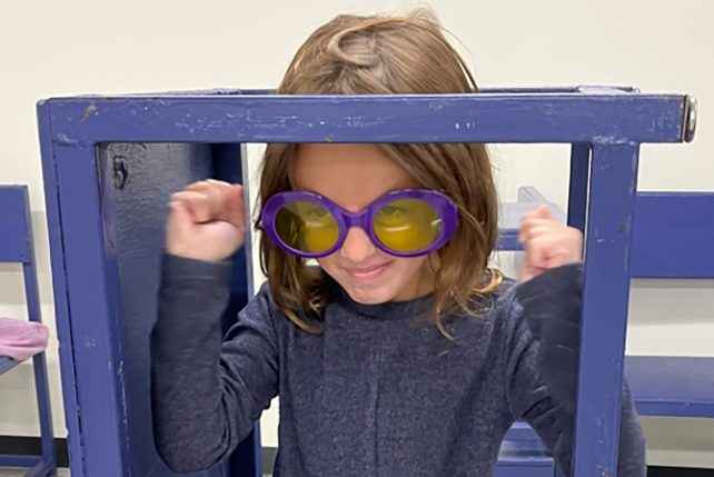 A child wearing purple glasses inside of a purple frame performs during the Saturday Morning Visual Arts and Creative Drama program.