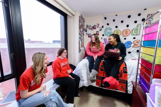 Four Illinois State University University Housing Services residents sit in a residence hall room and chat.