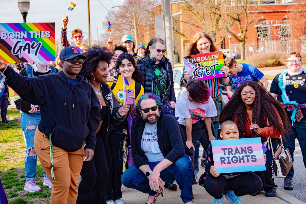Queer Coalition members and allies pose for a group photo during last March's Trans Day of Visibility Sashay. Members are holding signs which read "Born this gay," "I'm rollin' with the LGBT," and "Trans rights."