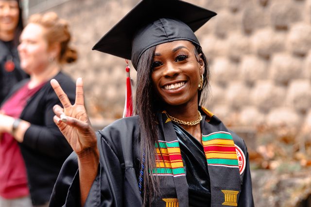 student wearing cap and gown and showing the peace sign with her fingers