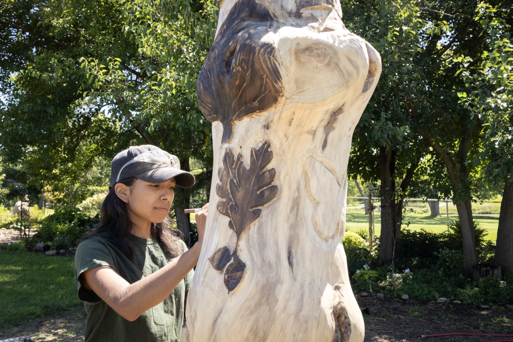 A woman carves into a tree trunk.