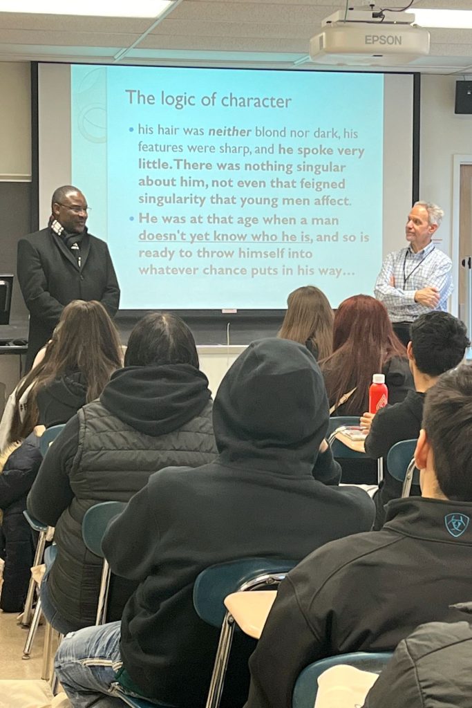 Interim President Aondover Tarhule, left, and Dr. James Pancrazio, a professor of Spanish, right, stand between a screen at the front of a class with students.