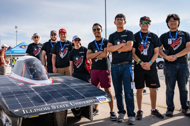 Members of the Illinois State University Solar Car Team stand smiling next to their car.