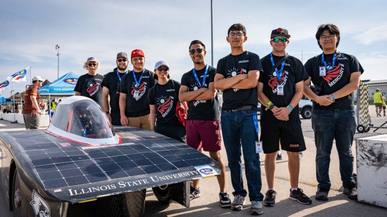Members of the Illinois State University Solar Car Team stand smiling next to their car.