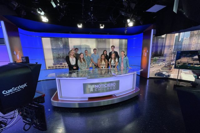A group of student interns standing behind the NBC desk.
