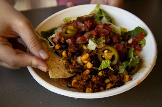 Bowl of nachos with meat, corn, beans, lettuce, and salsa with a hand dipping a chip.