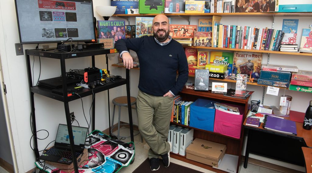 Dr. Sercan Şengün in front of bookshelves filled with games