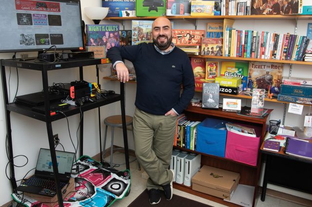 Dr. Sercan Şengün in front of bookshelves filled with games