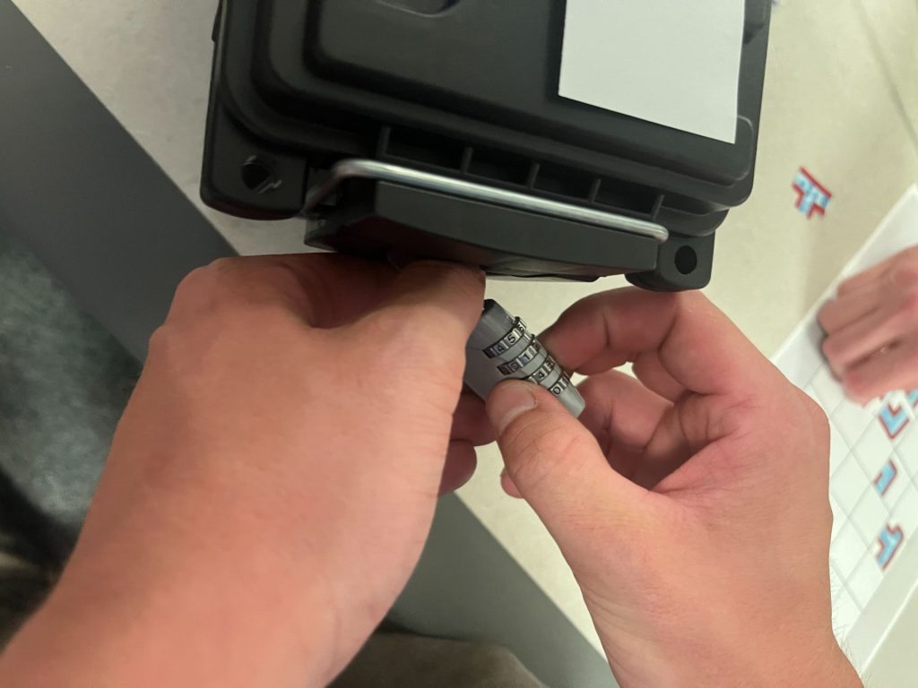 Two hands work to open a lock attached to a box.