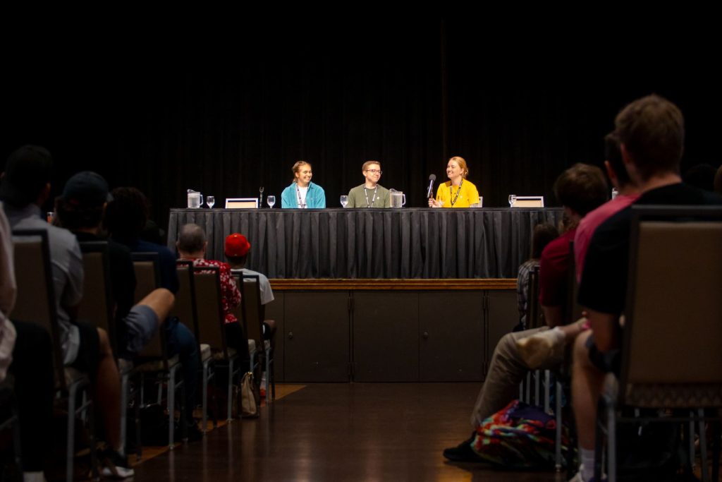 Three people sit behind a table on a stage.