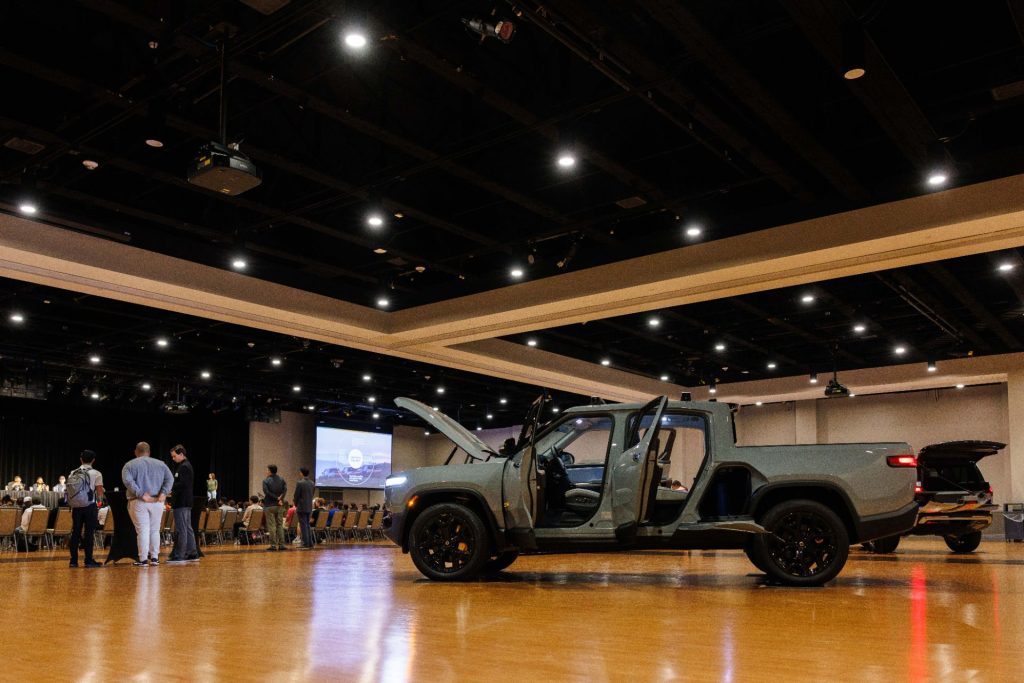 A Rivian R1T is parked in the Brown Ballroom with all of its doors open, as people in the background listen to a panel discussion
