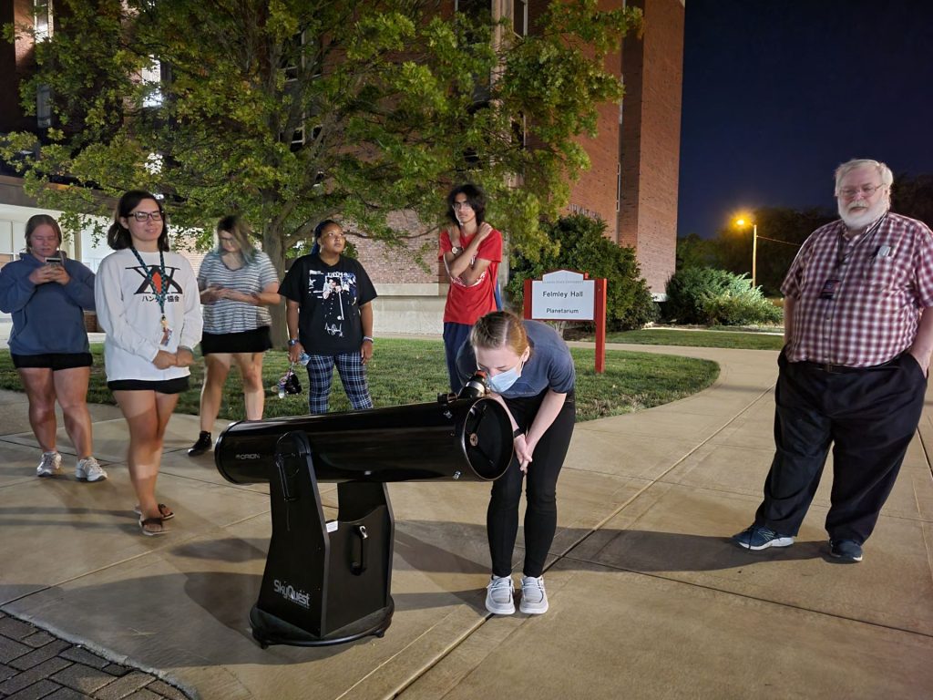 A group of students uses a telescope to view the night sky