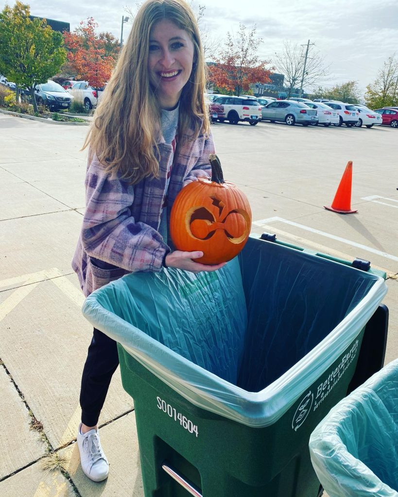 Student holding a pumpkin carved with a Harry Potter image near green compost bins.