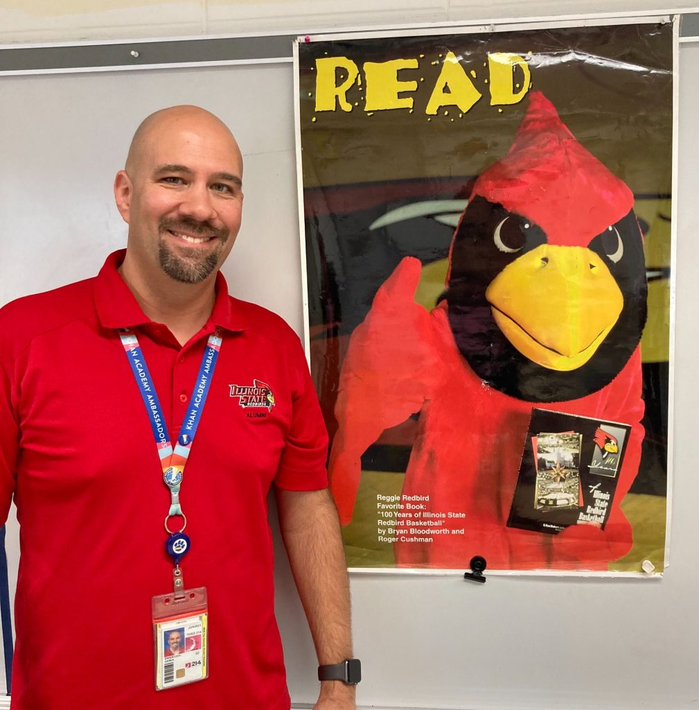 person wearing illinois state polo shirt standing next to poster with Reggie Redbird encouraging people to read