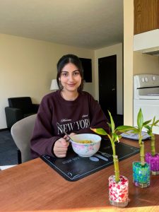 Girl sitting at table in kitchen with bowl of food and bamboo plants in front of her