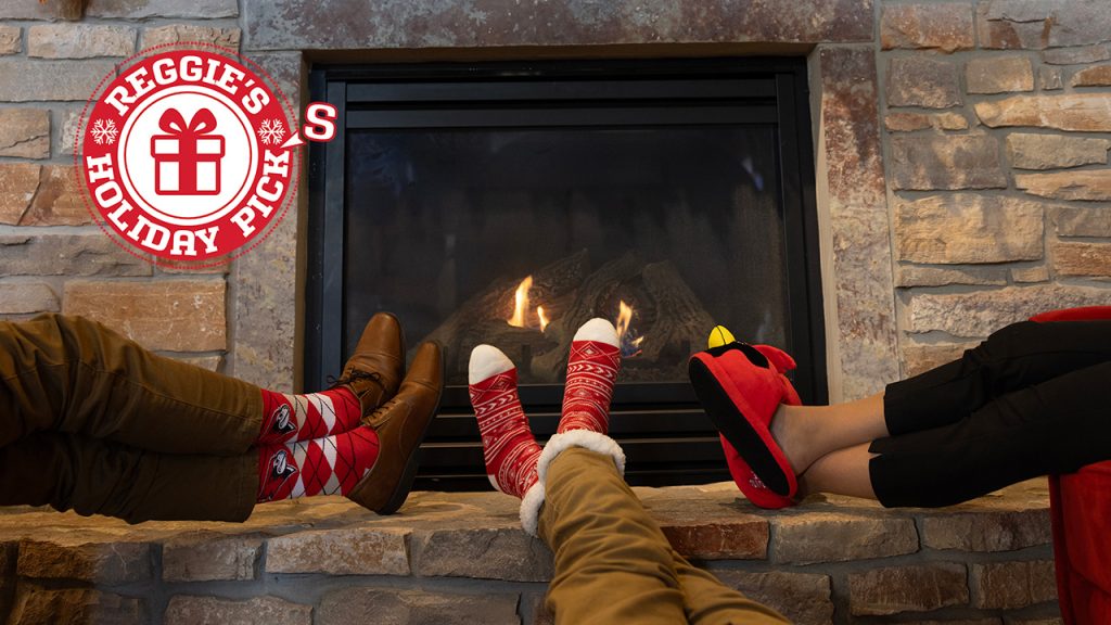 Three pairs of feet propped by the fire with a logo that reads "Reggie's Holiday Picks"
