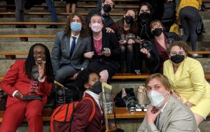 students wearing surgical masks pose for a picture sitting in bleachers
