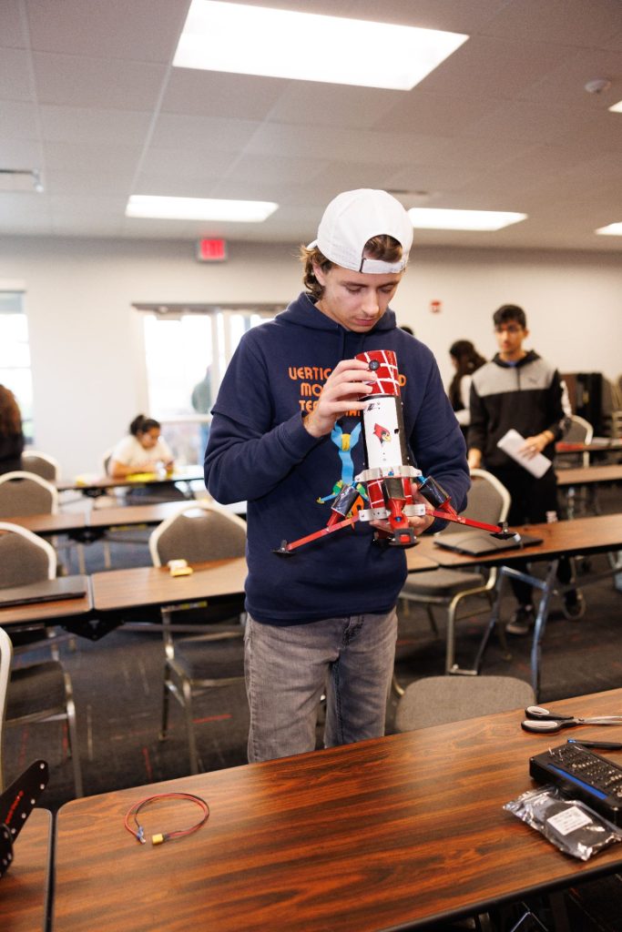 A student holds a rocket with a Reggie Redbird logo on it, in a classroom