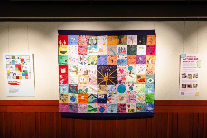 A multicolored quilt and corresponding exhibit hanging on the wall at Milner Library.