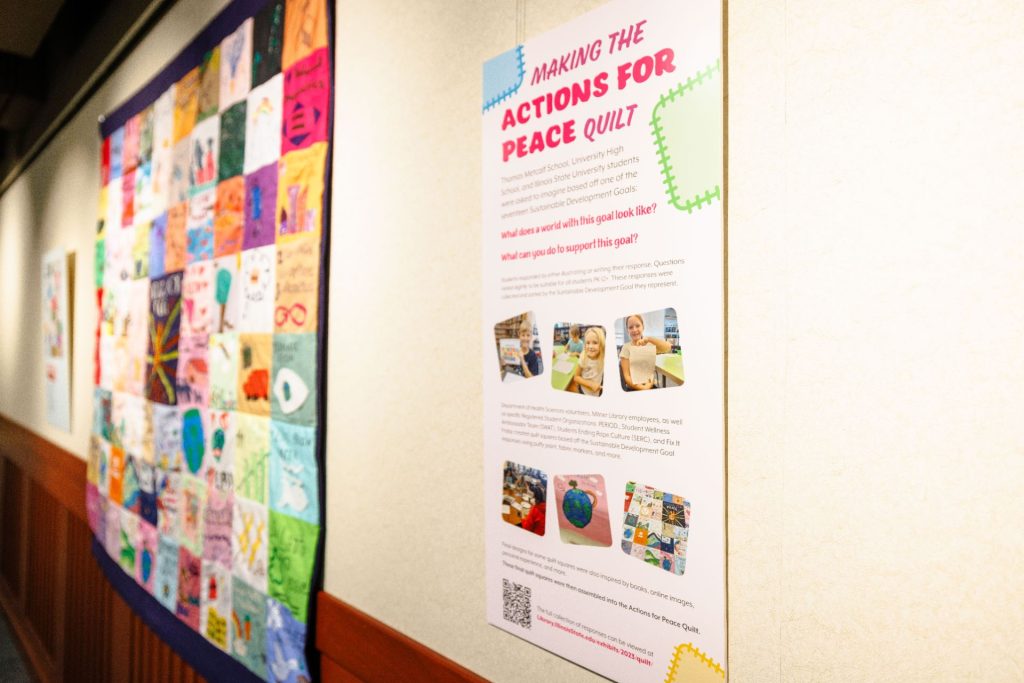 A quilt and corresponding exhibit hanging on the wall at Milner Library. A poster near the quilt reads "making the actions for peace quilty"