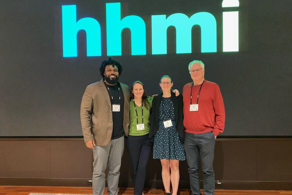 Dr. Keenan Wimbley (left), Dr. Rebekka Darner, Dr. Lisa Tranel, and Dr. Dan Holland standing in front of the HHMI logo