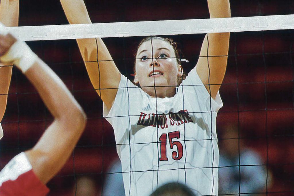 A Redbird volleyball player lifts arms above net to attempt a block