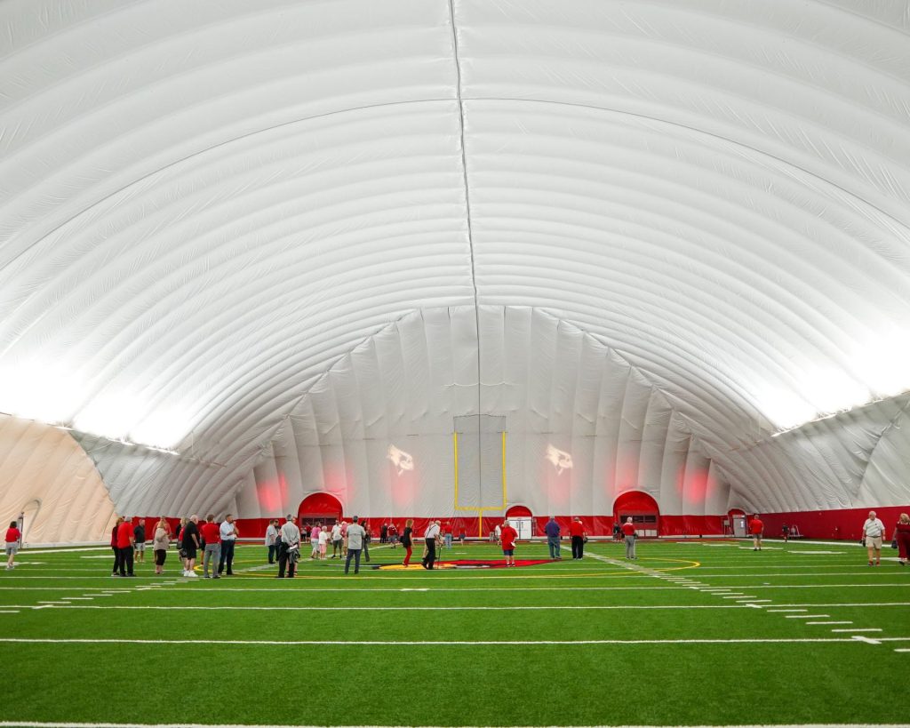 Interior view of people walking on turf under an inflatable roof.