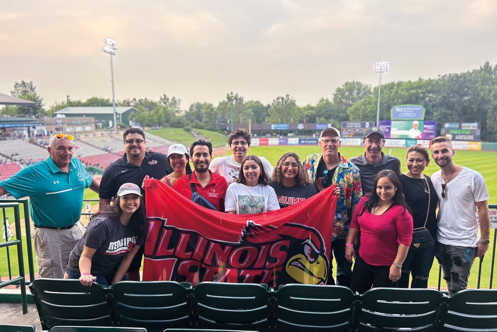 Latinx alumni group holding Illinois State flag at a baseball game.