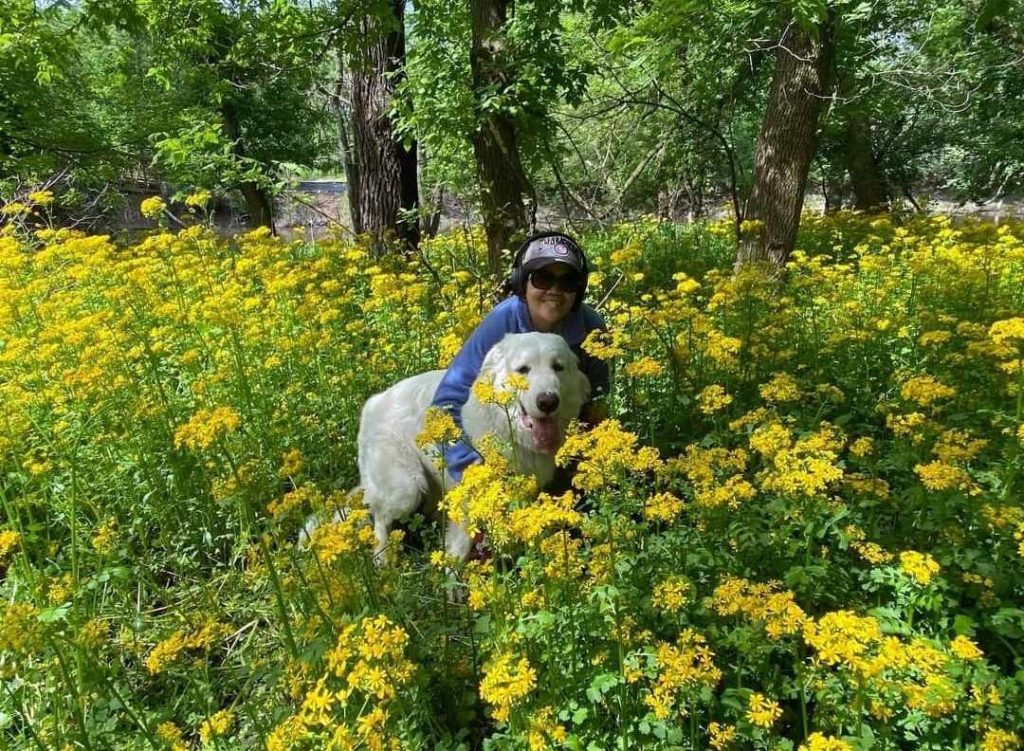 Reyes crouches in tall flowers outdoors with her dog, a Great Pyrenees.