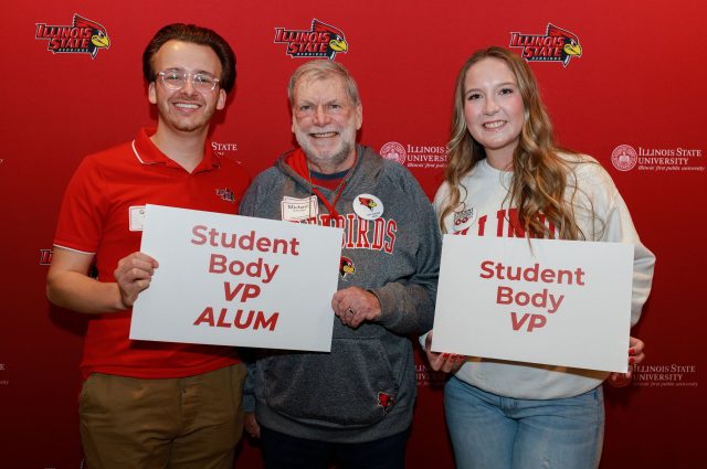 one current student government representative poses with two student government alumni holding signs reading "student body VP alum" and "student body VP"