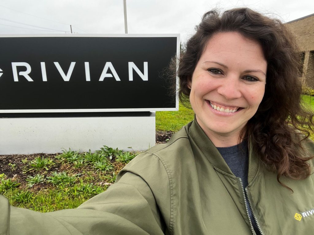 Woman standing in front of a sign that says "RIVIAN."