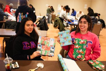 Two students holding up wrapped presents and smiling