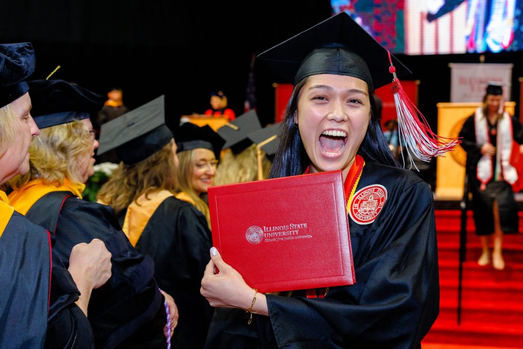 women holding up diploma at commencement with big smile