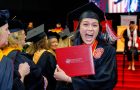 women holding up diploma at commencement with big smile