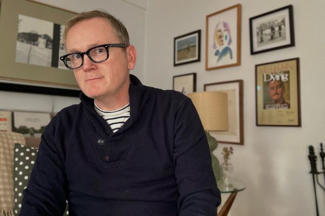 Pat Healy sitting in a room in front of framed photos and a lamp