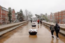 Students walk across the College Avenue bridge in the winter with snow on the trees.