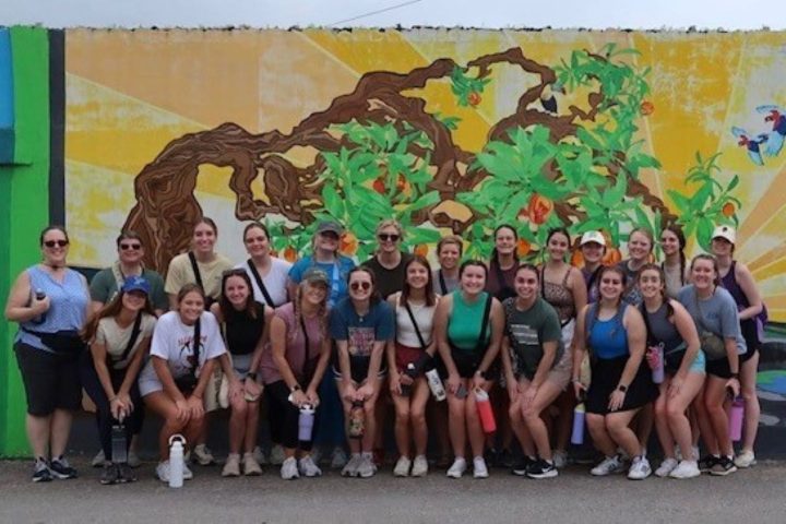 CSD students are grouped for a photograph in front of a colorful mural in San Ignatio, Belize