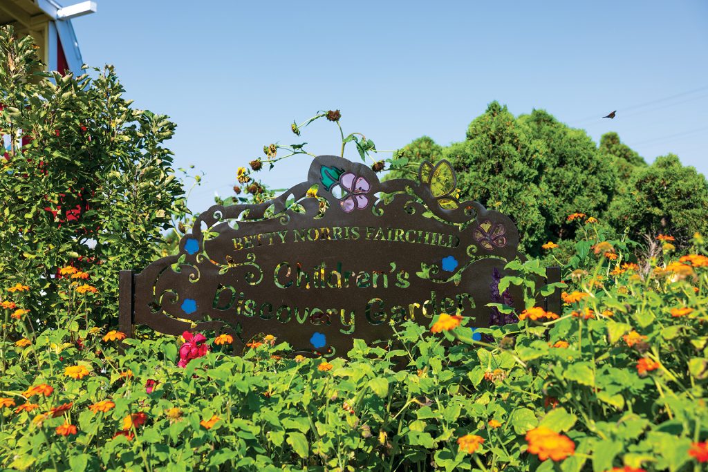 a sign in a garden surrounded by greenery
