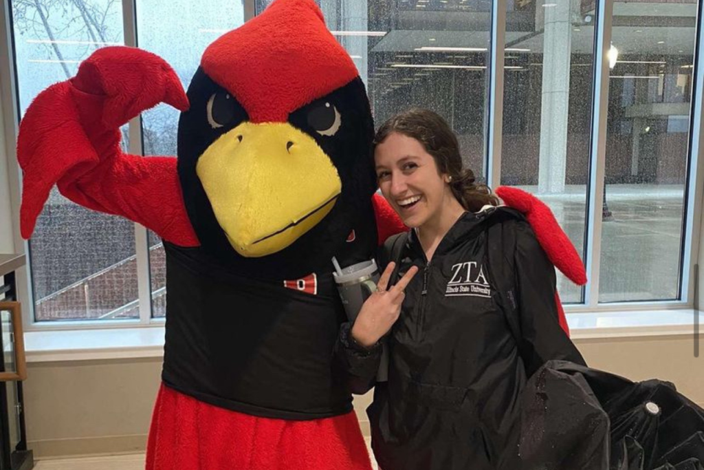 girl holding up peace sign and standing next to Reggie Redbird mascot