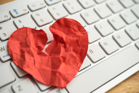 Crushed and ripped red paper heart resting on a keyboard.